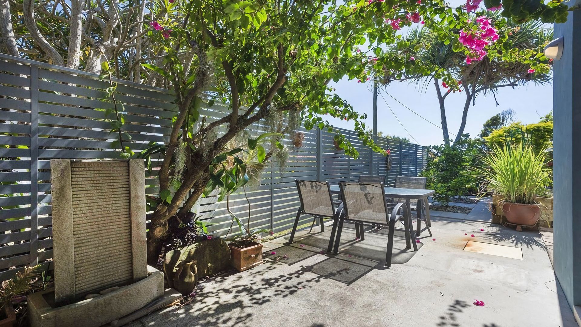 A patio area with a table and chairs, a potted plant, and a fence.