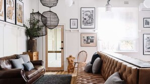 A modern living room with a leather sofa, a wooden chair, and a long bench. There are framed artworks on the walls and a hanging light fixture. - The Oxford ~ Hepburn Springs/Daylesford ~ Sleeps 24 (Hepburn Springs)