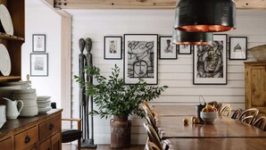 A dining area with a wooden table, chairs, a vase with green plants, and framed artwork on the wall. - The Oxford ~ Hepburn Springs/Daylesford ~ Sleeps 24 (Hepburn Springs)