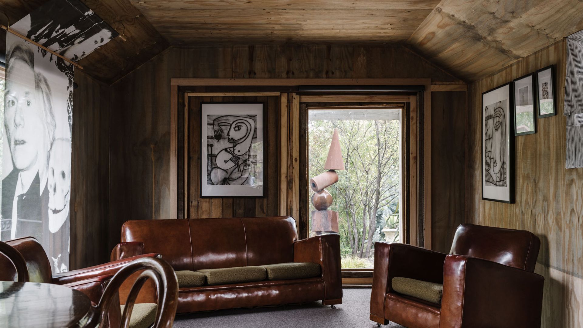 A wooden interior with a leather sofa, a chair, and framed artwork on the walls.