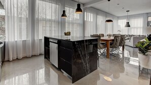 A modern kitchen with a black marble island, a dining area with a wooden table and chairs, and a living room with a sofa and a coffee table. - THE BOHO CHIC | Two-Bedroom Loft w. Terrace (Montréal)