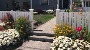 A two-story house with a front yard, a white picket fence, and a paved walkway leading to the entrance.
