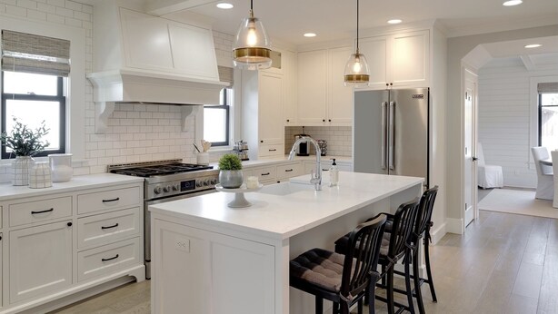 A spacious kitchen with white cabinetry, a large island with bar stools, a stainless steel refrigerator, and pendant lighting.