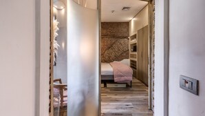 A modern bedroom with a wooden floor, a bed with a pink blanket, and a brick accent wall. - Suite Trastevere San Calisto Rome Historical Center  (Roma)