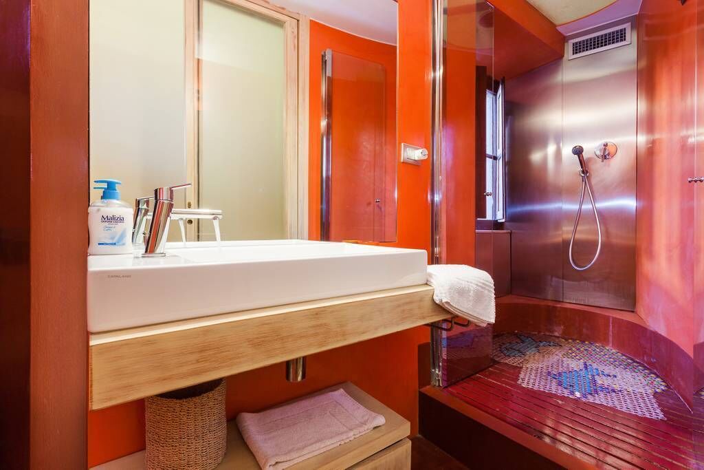 A bathroom with a white sink, a mirror, a shower with a glass door, and a towel on the floor.