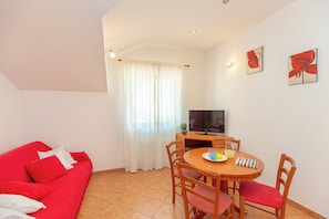 A living room with a red sofa, a wooden dining table with chairs, a television, and a window with curtains. - Apartment Mondo A2 - One Bedroom Apartment, Sleeps 2 (Mokosica)
