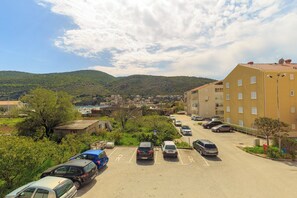 A parking lot with several cars, a building with multiple windows, and a mountainous backdrop. - Apartment Mondo A2 - One Bedroom Apartment, Sleeps 2 (Mokosica)