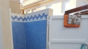 Ein gefliester Duschbereich mit blauem Mosaikmuster, eine weiße Tür mit einem darüberhängenden Handtuch und eine Minnie Maus Tasche an einem Haken.