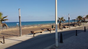 Eine Uferpromenade mit Holzbanken, Palmen und freiem Blick auf das Meer.