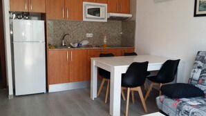 A compact kitchen with a white refrigerator, a microwave, and a sink. There is a dining table with four chairs and a sofa with a patterned cover. - Apartment in Cap Salou Area (Salou)