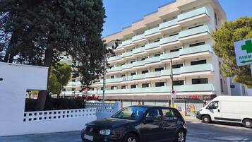 Un edificio de varios pisos con un letrero de farmacia, una camioneta blanca y un coche negro estacionados en la entrada.