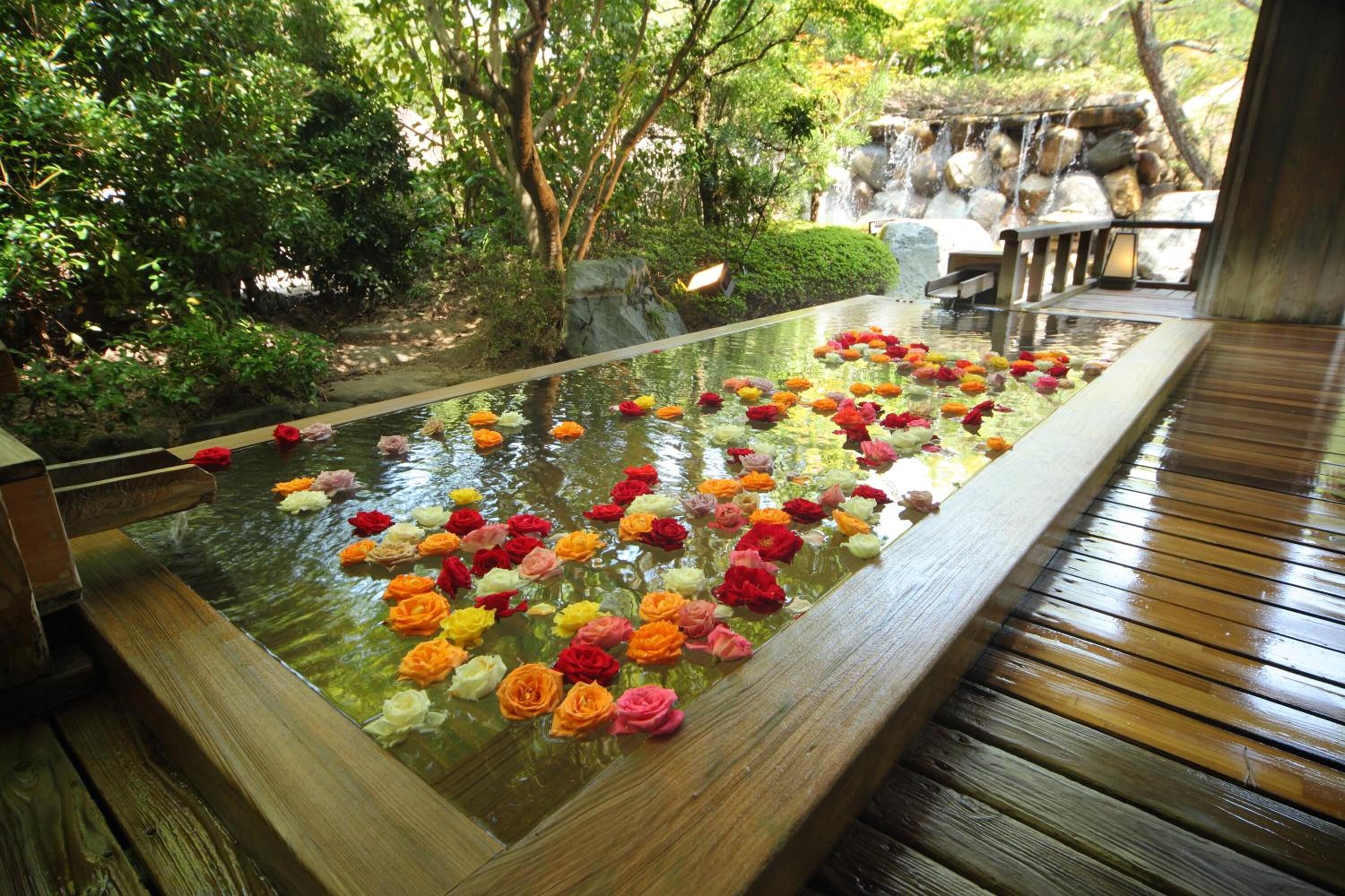 A serene indoor garden with a water feature, surrounded by lush greenery and a wooden deck.