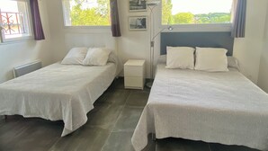 Ein Schlafzimmer mit zwei Betten, einem Nachttisch, einer Lampe und einem Fenster mit Vorhängen.