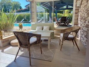 A sunlit patio with wicker furniture, a white sofa, and a view of a swimming pool. - Bassussarry: Apartment/ flat - BIARRITZ (Bassussarry)