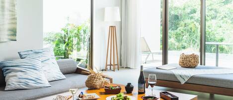 A modern living room with a dining table set for a meal, a sofa, and a large window with a view of greenery.
