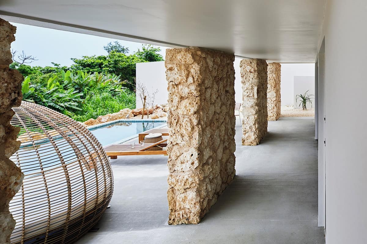 A modern interior with a pool, stone pillars, and a woven seating area.