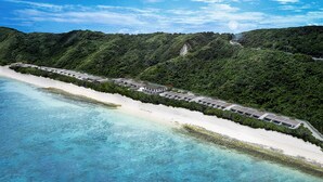 An aerial view of a resort with a long beachfront, lush green hills, and clear blue waters. - The Rescape (Miyakojima)