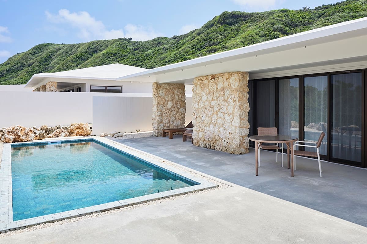 A modern house with a swimming pool, stone pillars, and a patio with chairs.