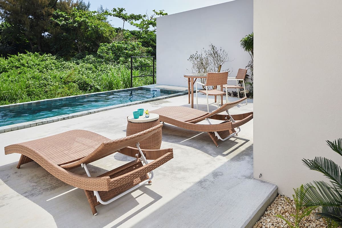 A poolside area with lounge chairs and a table, surrounded by greenery.