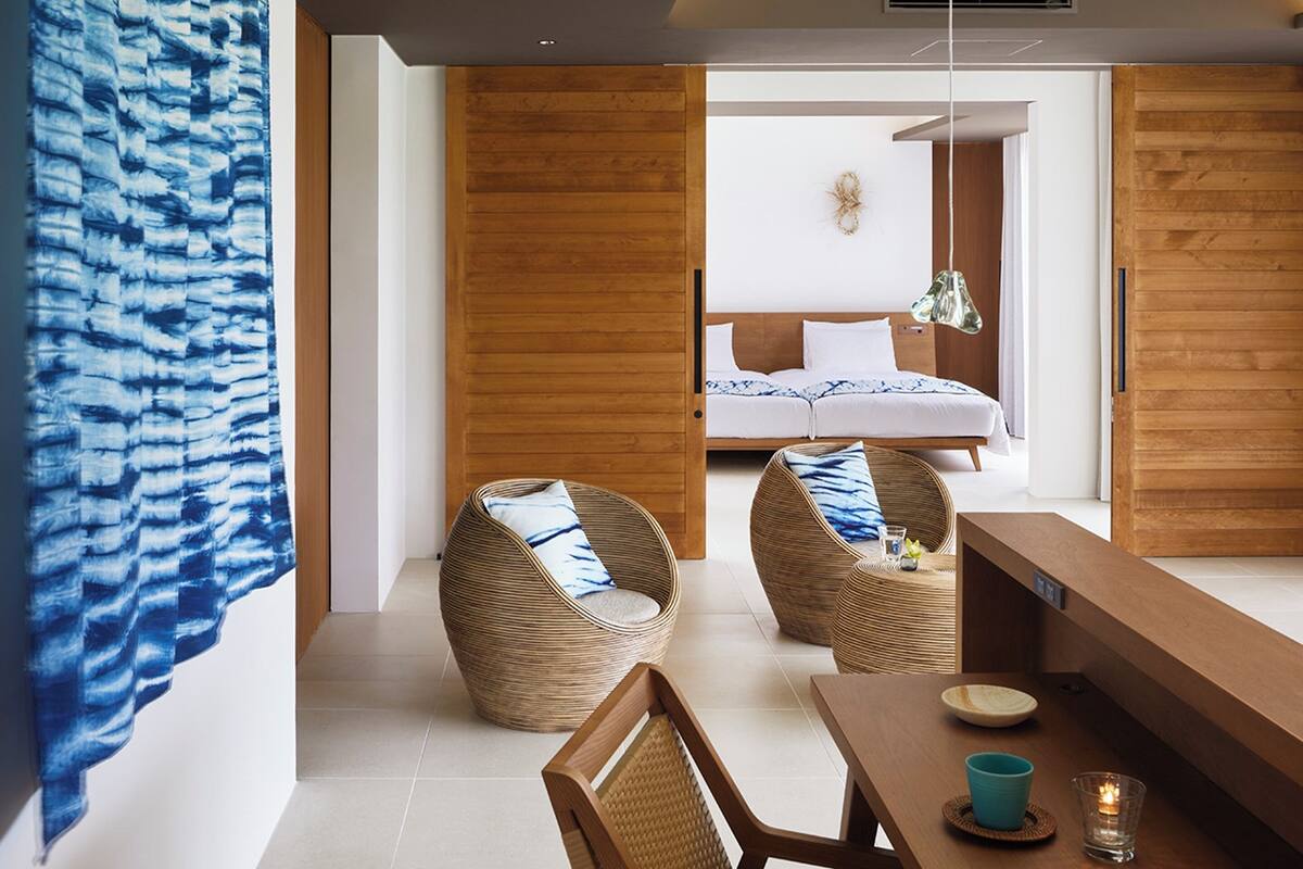 A modern room with a large bed, two wicker chairs, a wooden table, and a blue curtain.