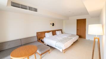 A hotel room with a bed, a sofa, a small table, a lamp, and a ceiling vent.