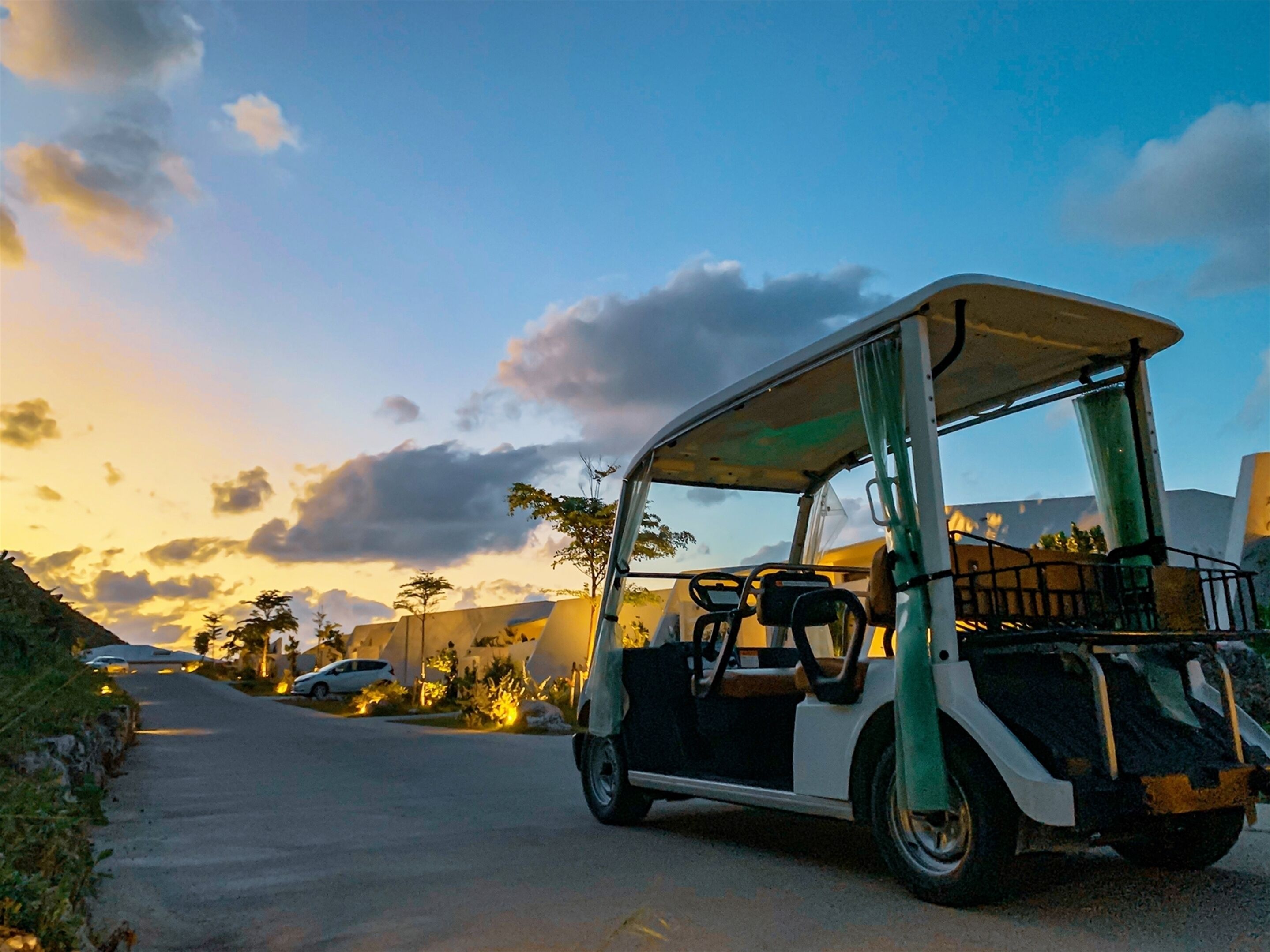 A golf cart parked on a road with a sunset in the background.