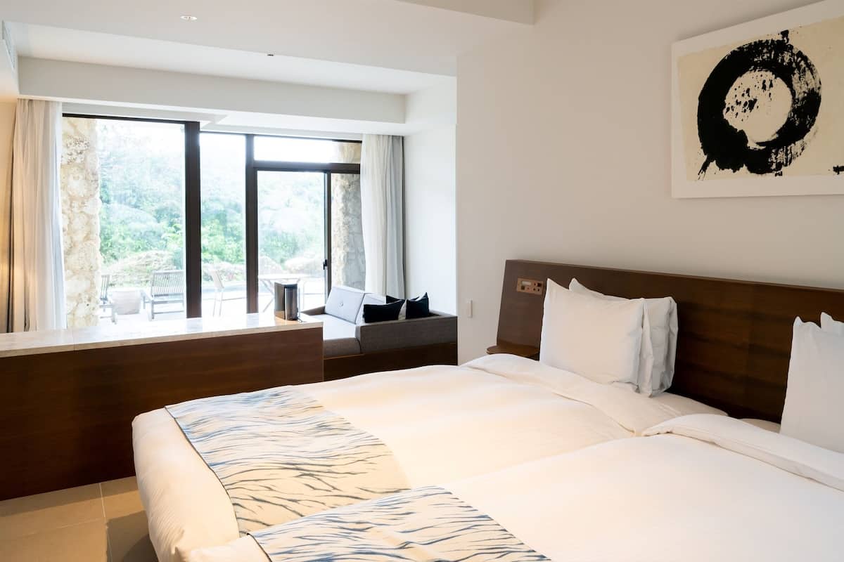 A hotel room with a large bed, a view of the outdoors, and a painting on the wall.