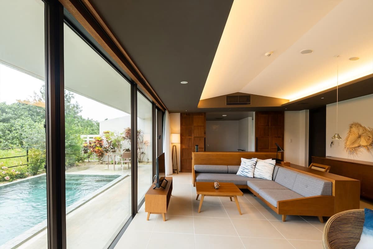 A modern living room with a large window, a sofa, a coffee table, and a dining area.