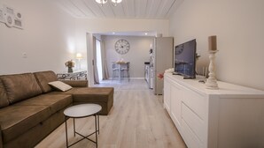 A modern living room with a brown sofa, a small round table, a TV on a white cabinet, and a chandelier. - Large 5 * Villa with heated pool and swimming pool in winter in St Gilles (Saint-Gilles les Bains)