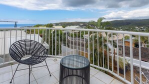A balcony with a black chair and a glass table, overlooking a coastal town and hills. - Large 5 * Villa with heated pool and swimming pool in winter in St Gilles (Saint-Gilles les Bains)