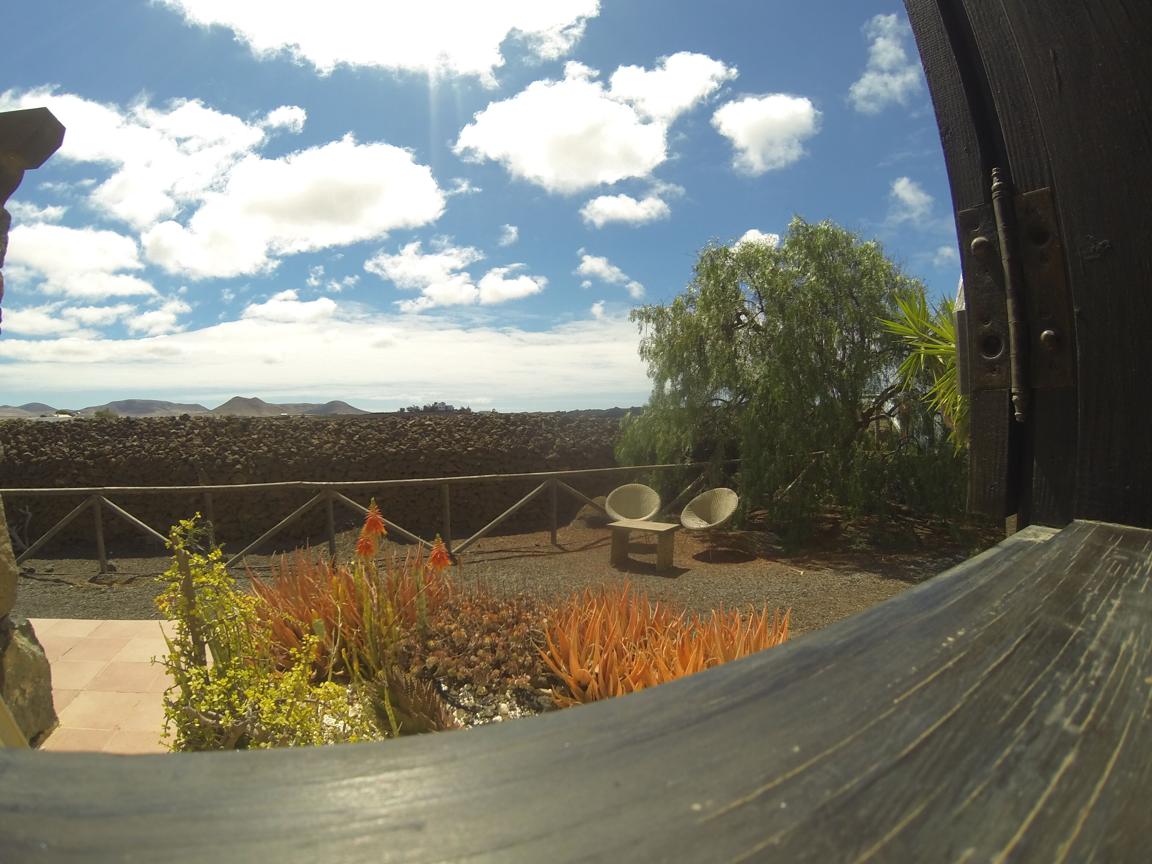A terrace with wicker chairs and a view of a rocky landscape under a partly cloudy sky.