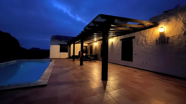 A poolside area with a pergola, outdoor seating, and a stone wall with a light fixture.