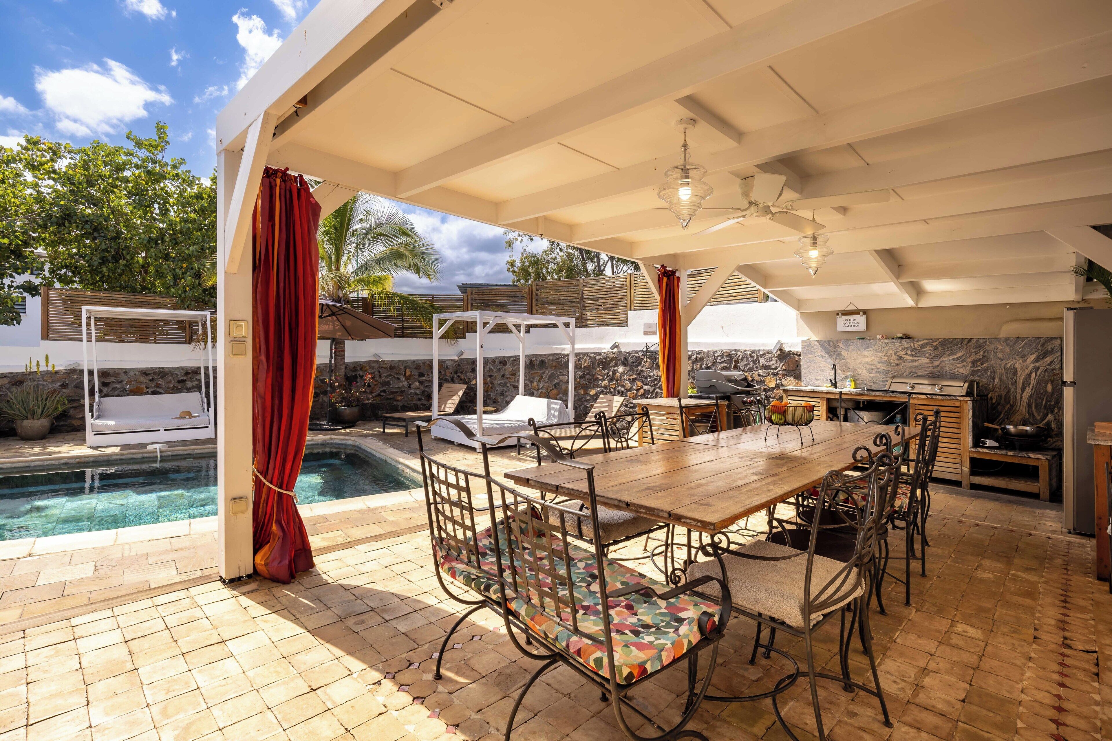 An outdoor patio with a pool, a wooden table, and chairs.