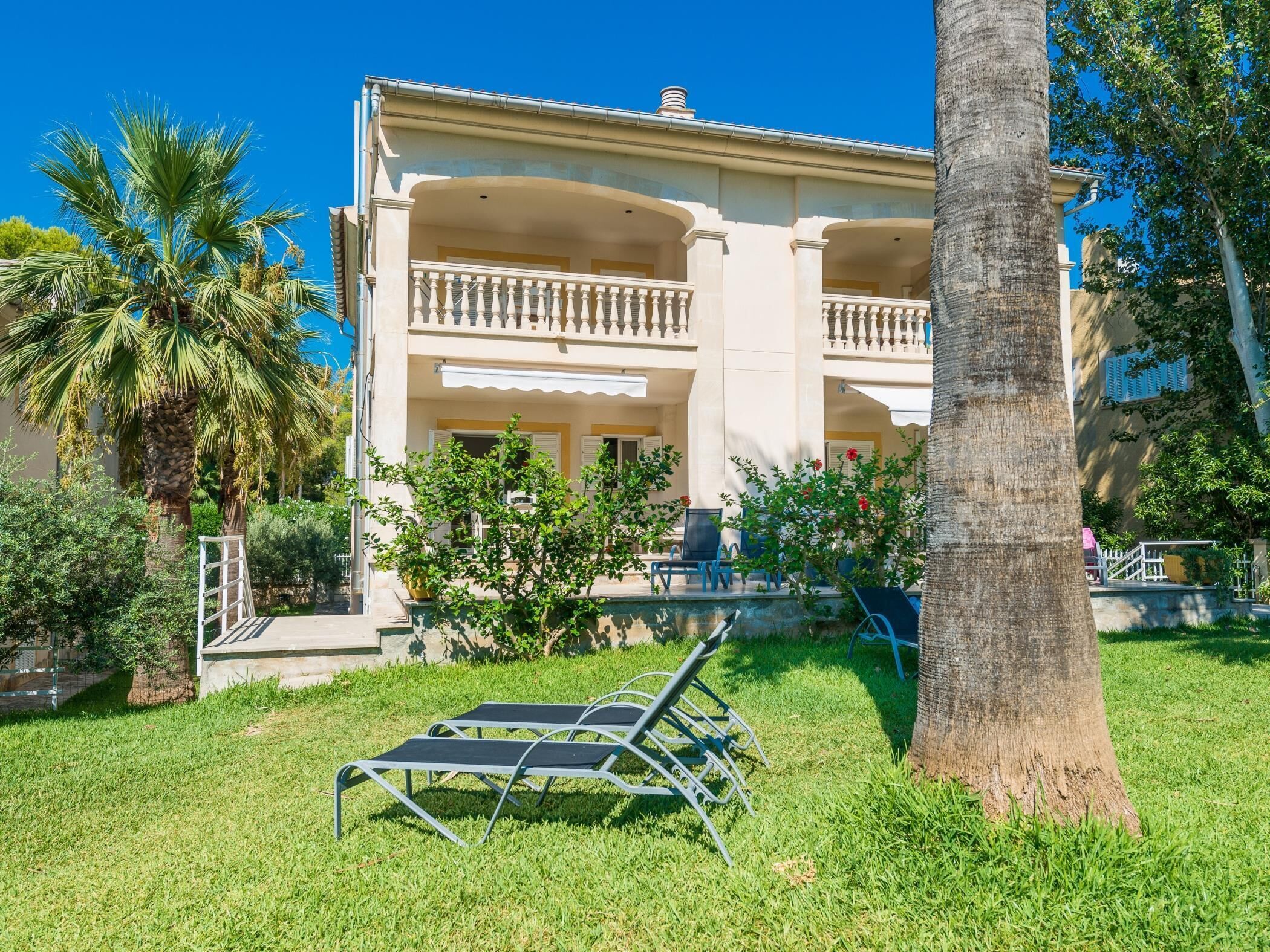 A two-story building with a balcony, surrounded by greenery and palm trees.