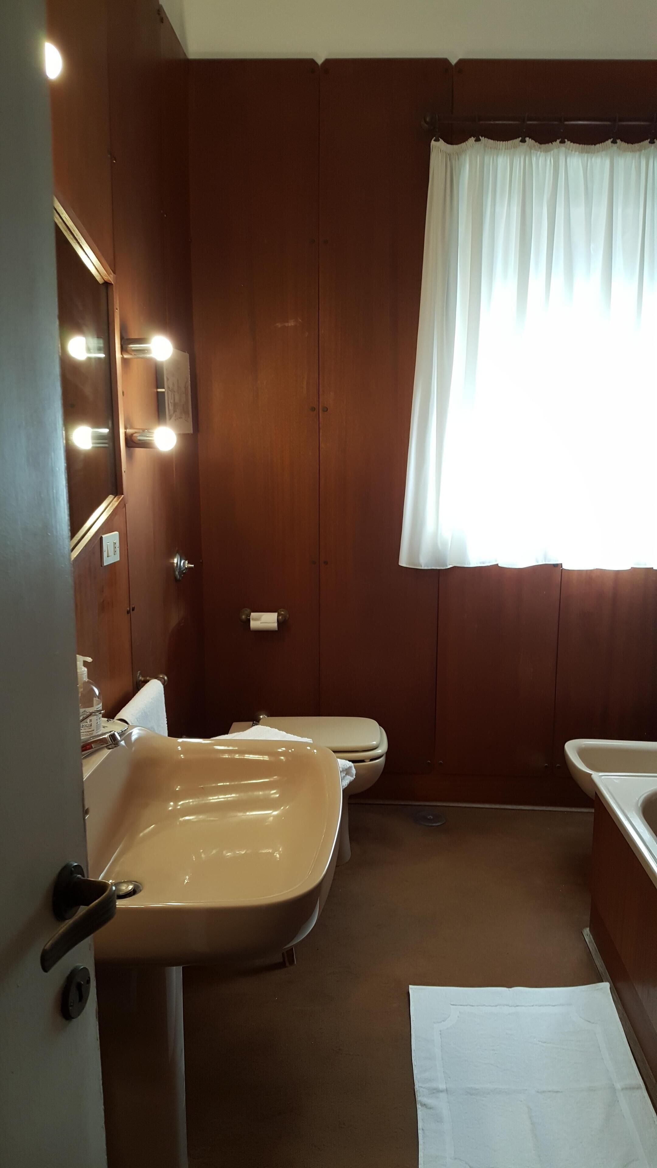 Ein kleines Badezimmer mit einem beigefarbenen Waschbecken, Toilette und einem beleuchteten Spiegel.