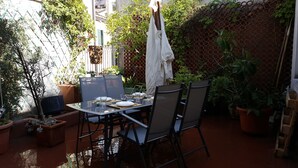 An outdoor patio with a table set for two, surrounded by chairs, potted plants, and a lattice fence. - Large apartment big lounge fireplace two terraces (Venezia)