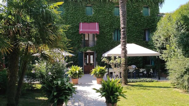 A building with a green ivy-covered facade, a red awning, and a covered outdoor seating area with tables and chairs. - MANOR HOUSE near Venice, Prosecco hills, and Dolomites with private pool (Codognè)