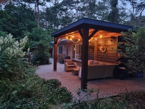 A covered patio area with a wooden structure, outdoor seating, and a brick pathway. - Lovely house near the forest and heath in Otterlo (Otterlo)