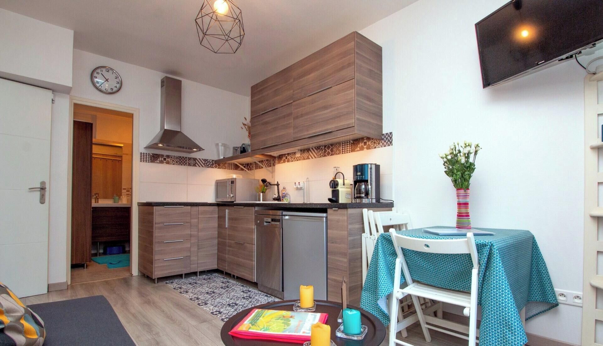 A compact kitchen with modern appliances, a dining area with a table and chairs, and a clock on the wall.