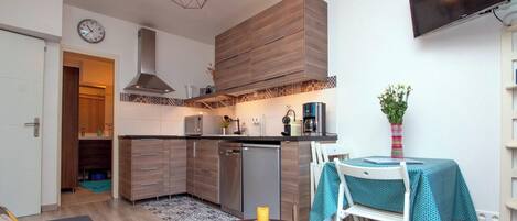 A compact kitchen with modern appliances, a dining area with a table and chairs, and a clock on the wall.