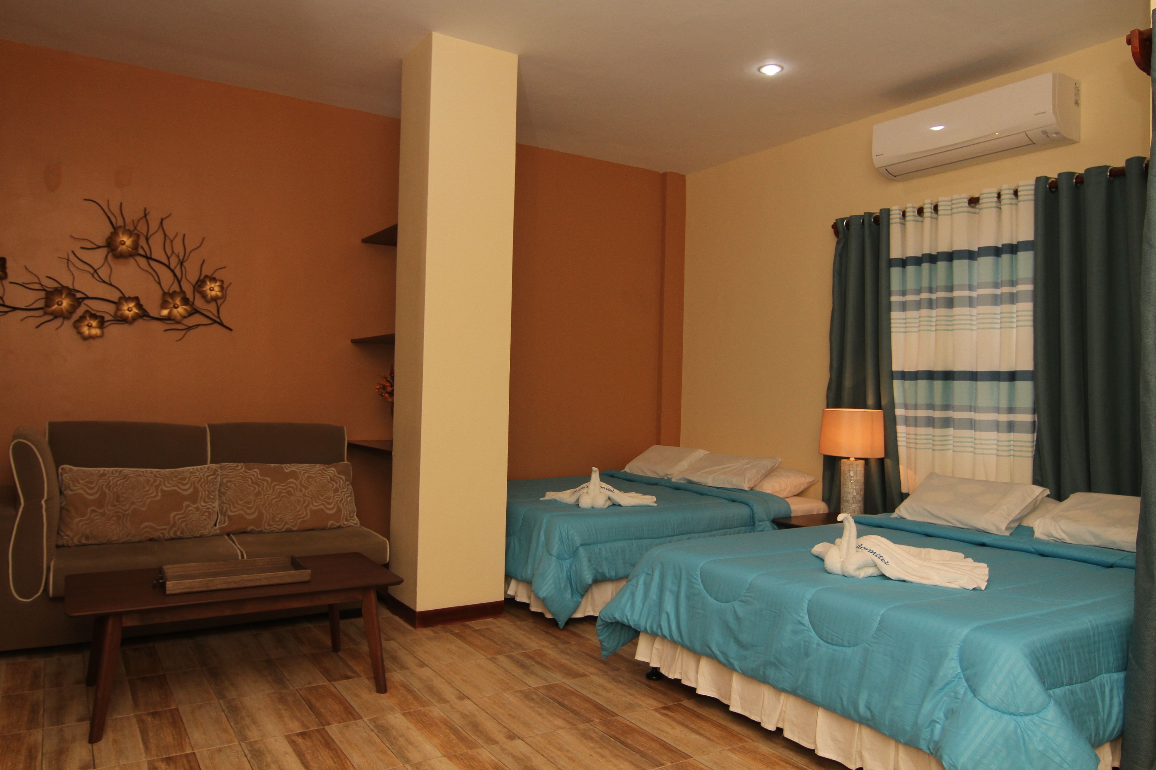 Une chambre d’hôtel avec deux lits, un canapé, un plancher en bois, un climatiseur et un élément décoratif mural.