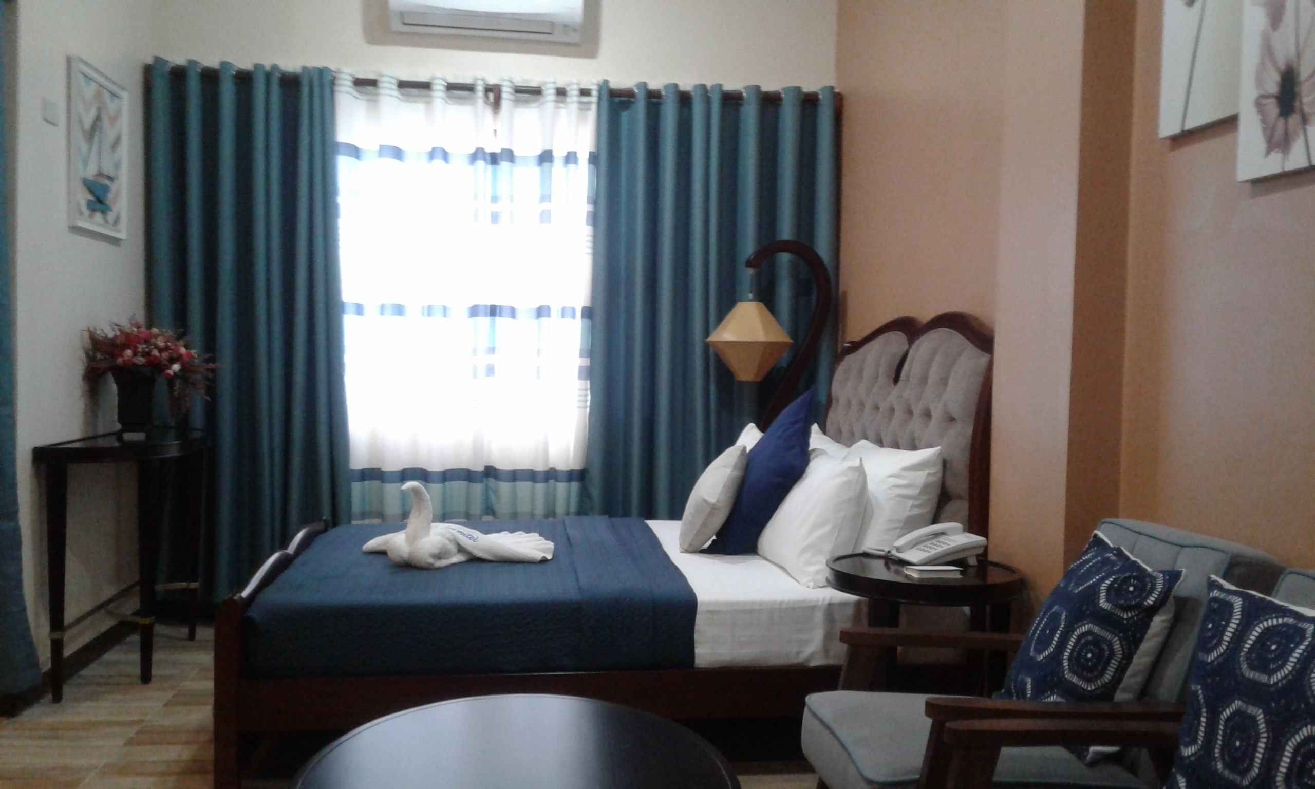 A hotel room with a bed, a bedside table, a chair, a lamp, and a window with curtains.