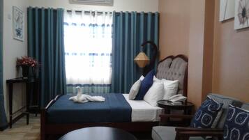 A hotel room with a bed, a bedside table, a chair, a lamp, and a window with curtains.