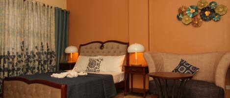 A hotel room with a bed, a sofa, a small table, and a wall decoration.