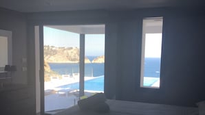 Un dormitorio con una cama grande, vista al mar a través de una puerta corredera y un ventanal pequeño.