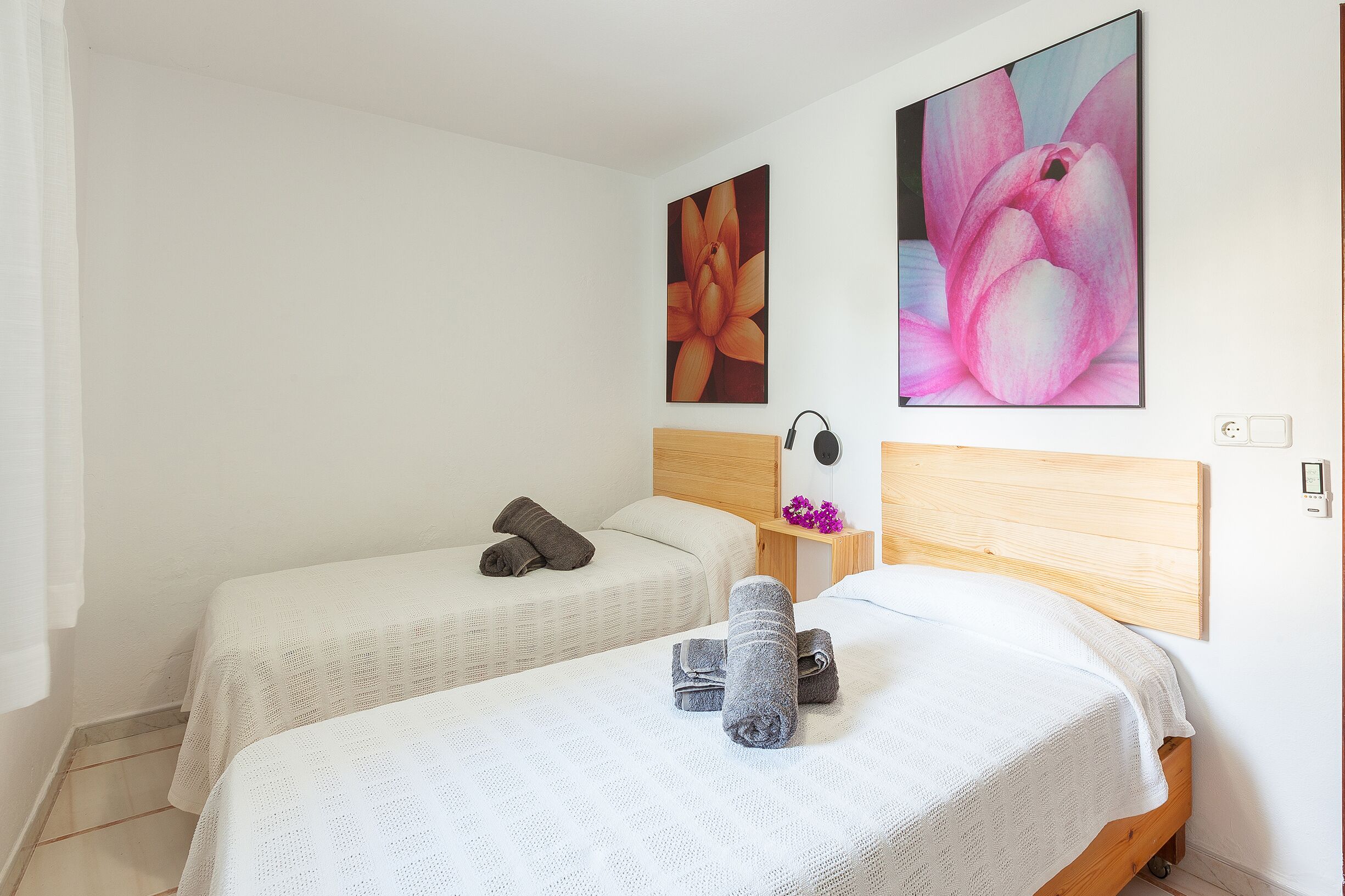 Habitación de hotel con dos camas, cada una con cubrecama y toallas blancos. Hay dos cuadros grandes con motivos florales en las paredes.