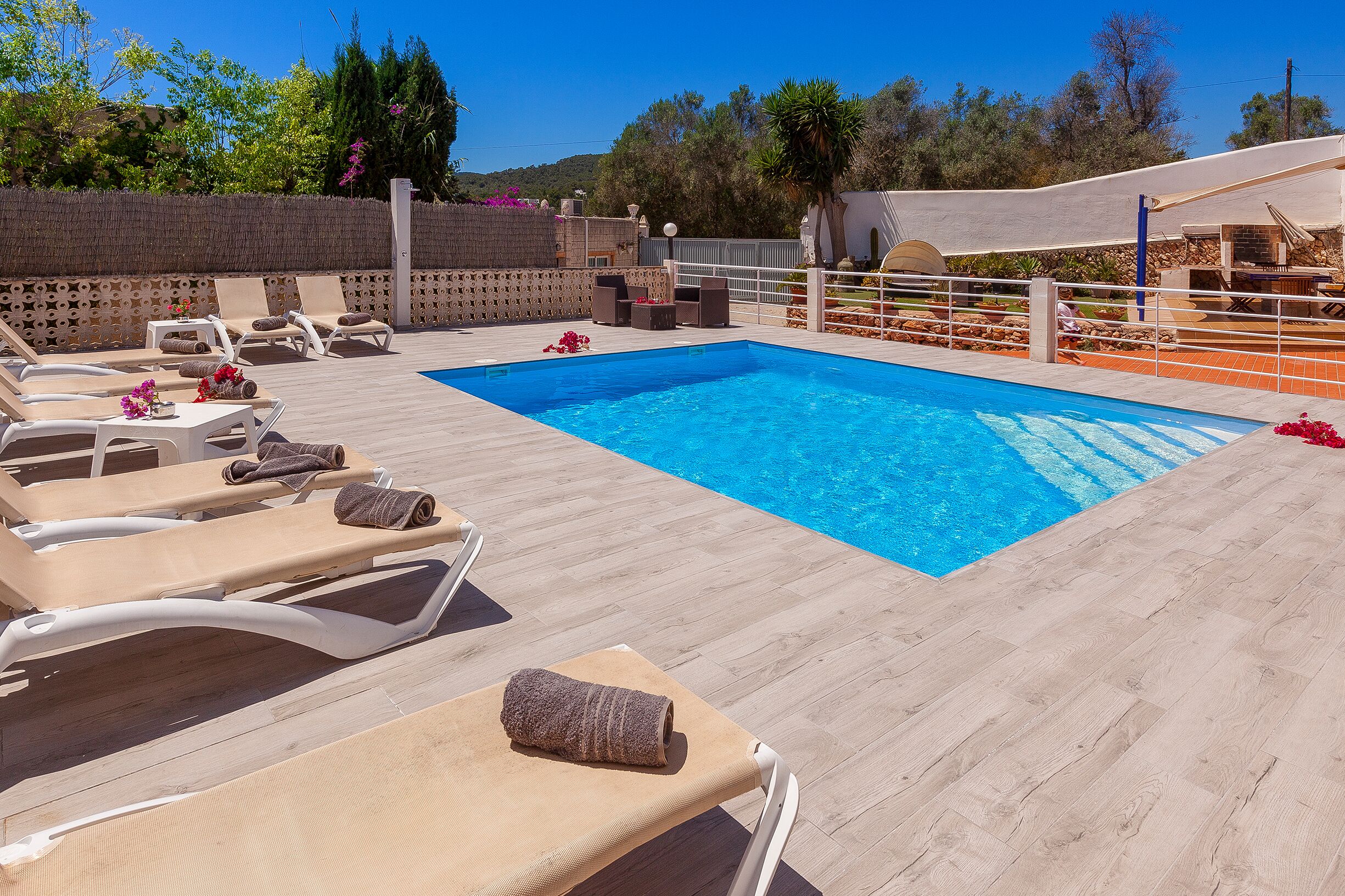 A pool area with lounge chairs and a small table, surrounded by a wooden deck and a white fence.
