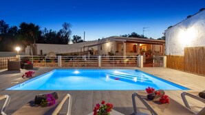 Una piscina con lettini e un tavolino con fiori, circondata da un solarium in legno e un recinto bianco.