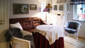 A cozy living room with a brown leather sofa, a wicker chair, a table with a lace tablecloth, and a patterned rug.