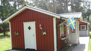 A red wooden cabin with a white door, a porch with a bench, and a flag.